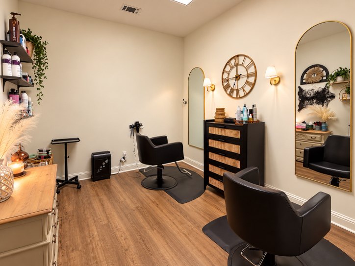 Private salon suite in Bogart GA with two black styling chairs, arched gold mirrors and wood floors