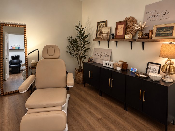 Lash extension suite with a tan treatment chair, black cabinets and wood shelving
